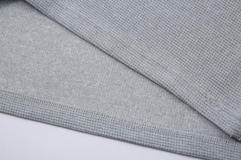 Close-up of light gray textured knit fabric with neat hem stitching on a half-zip graphic T-shirt