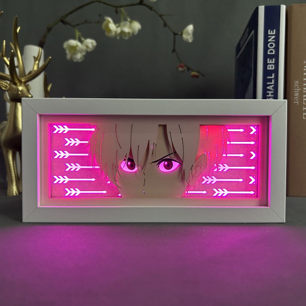 The Tokyo Revengers Anime Light Box – Ken Ryuguji (Draken) 3D LED Lamp features a vibrant illustration, focusing on eyes and hair against a pink background with arrow designs. It sits alongside books and a deer ornament.