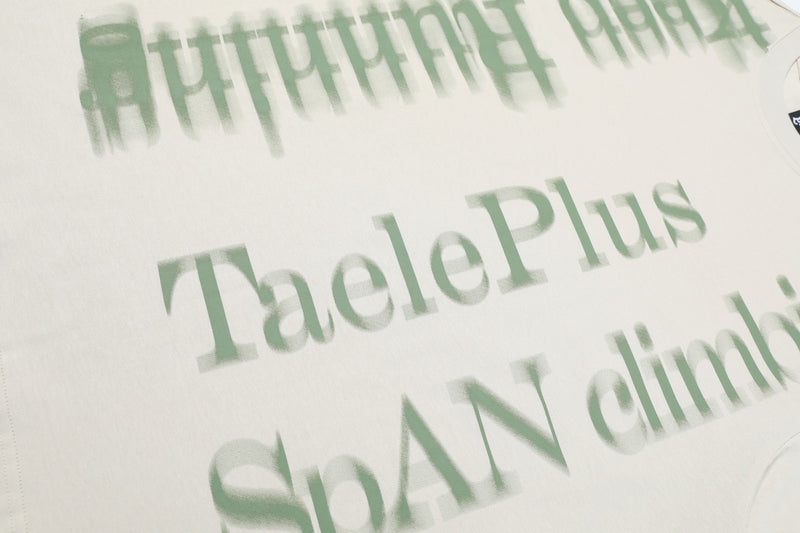 Close-up of a washed white oversized tee with faded green spray-letter graphic text and streetwear style print