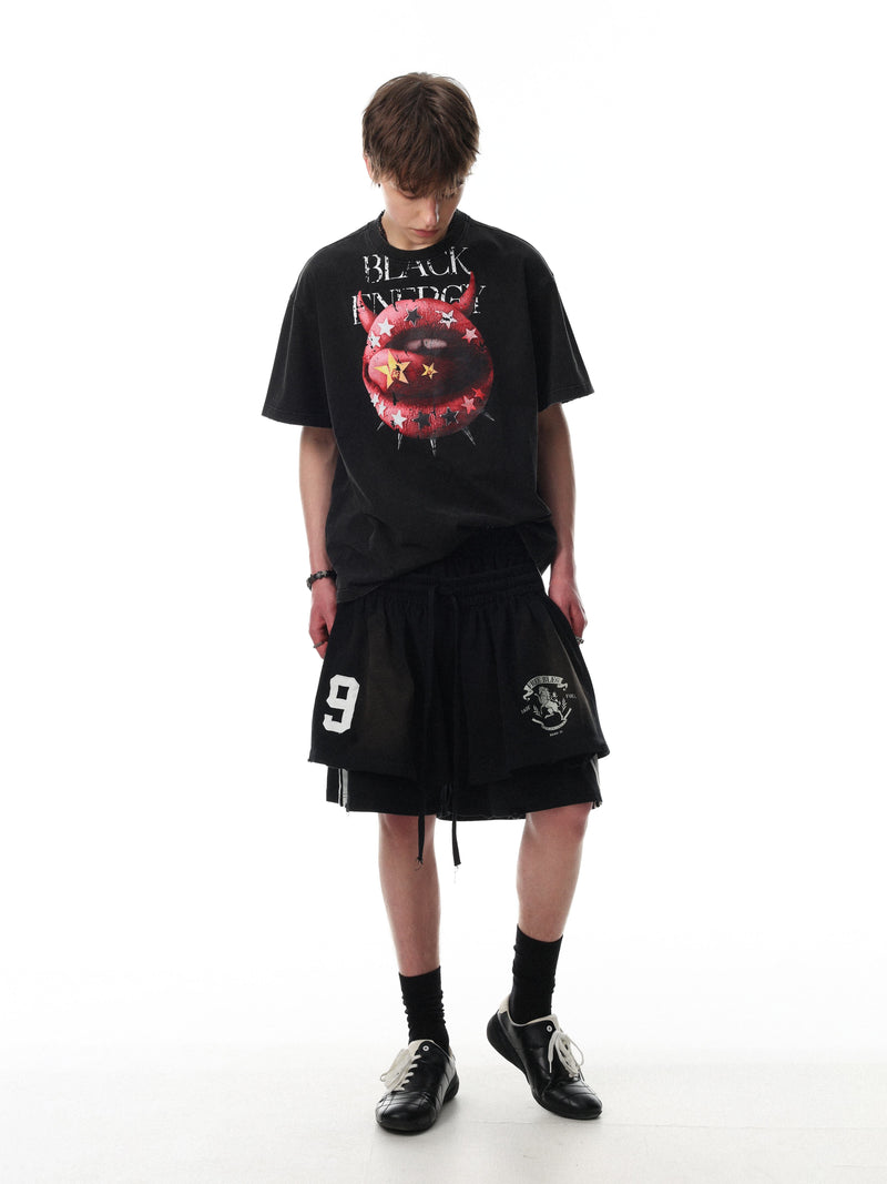 Black oversized graphic tee with red devil lips print, styled with black shorts and sneakers on a white background