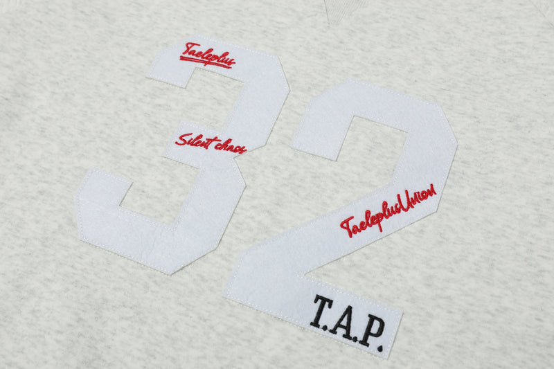 Close-up of white 32 graphic with red script and T.A.P. patch on heather gray sweatshirt