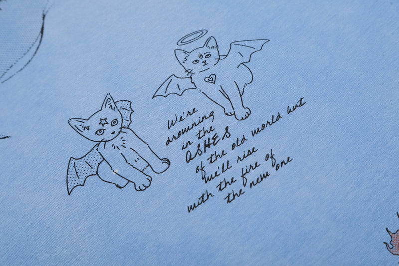 Light blue cotton tee with hand-drawn angel cat sketch and handwritten text graphic in black ink