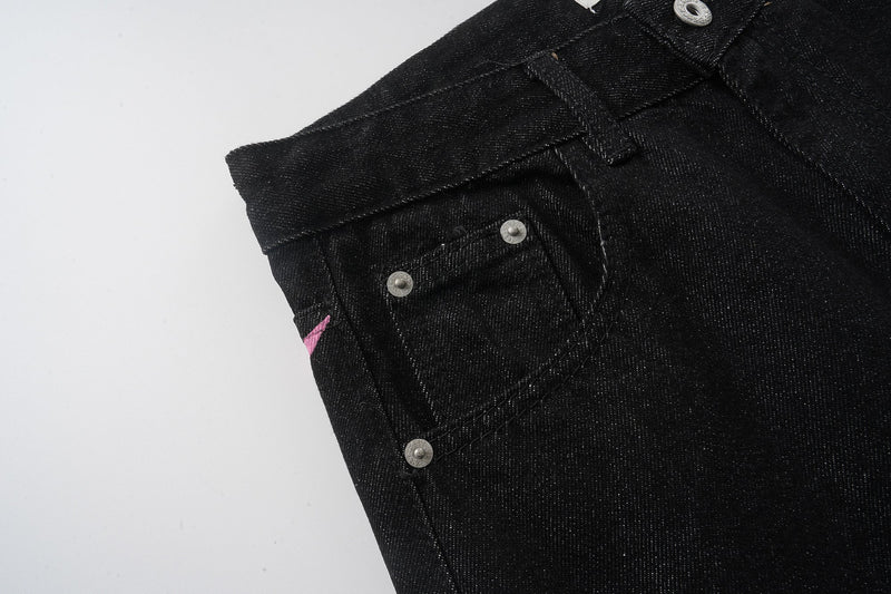 Back side close-up of black jeans with small pocket, rivets, and pink accent stitching
