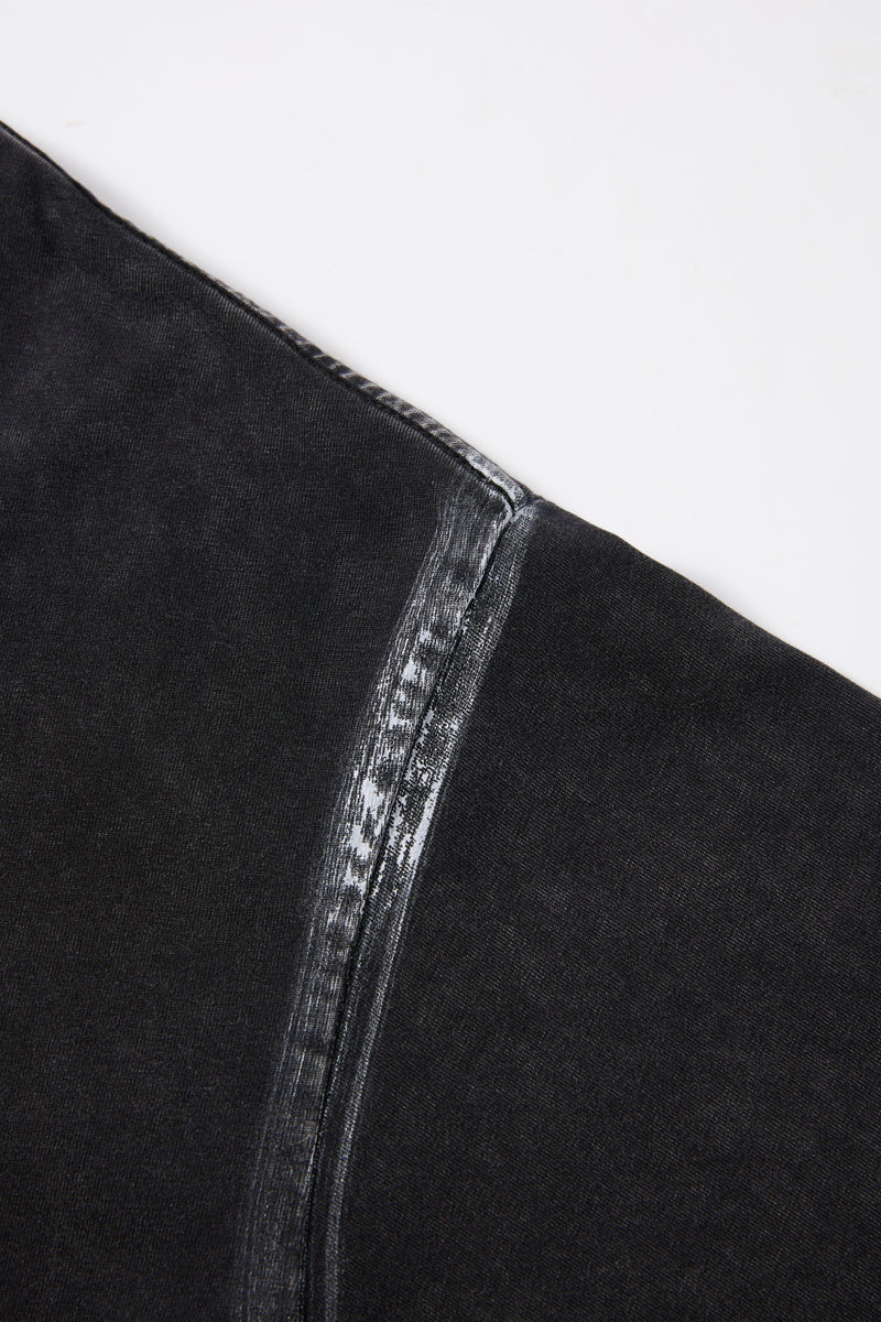Close-up of a black washed T-shirt seam with distressed spine graphic detail on dark streetwear fabric
