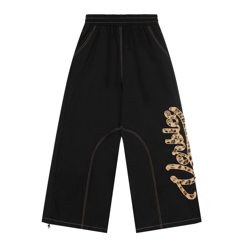 Black wide-leg pants with leopard patch lettering on one leg and contrast stitching, front view