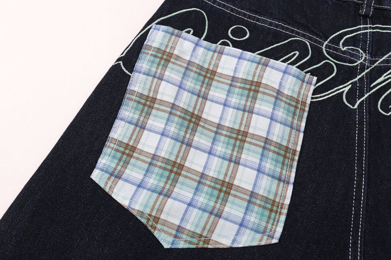 Close-up of plaid patch pocket on dark denim shorts with pale green outline stitching