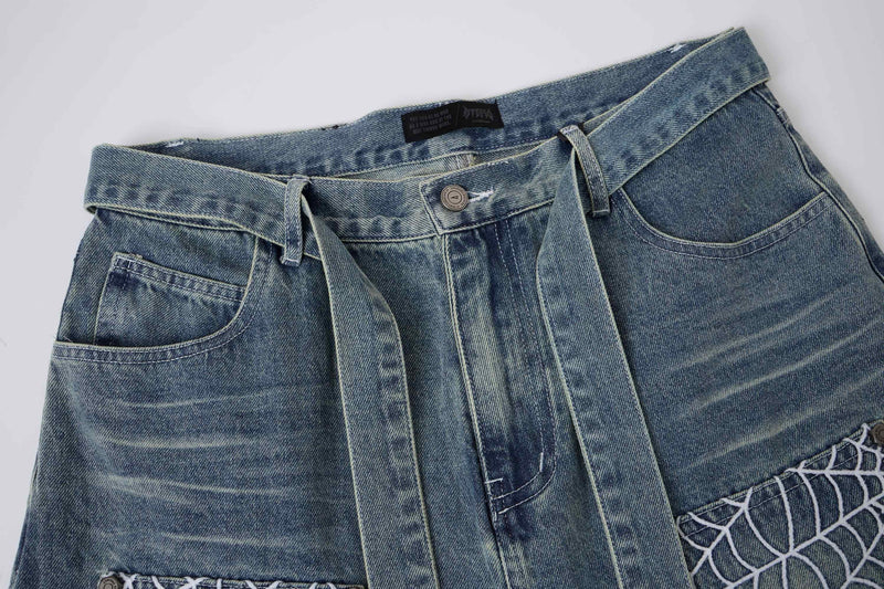 Close-up of light wash denim shorts front with hanging straps and spiderweb pocket panels