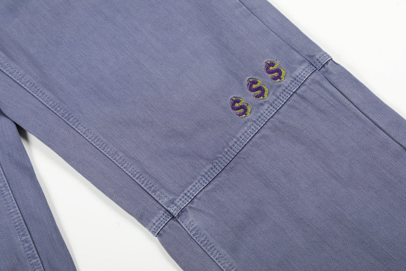 Close-up of blue carpenter pants showing three embroidered dollar signs on the leg