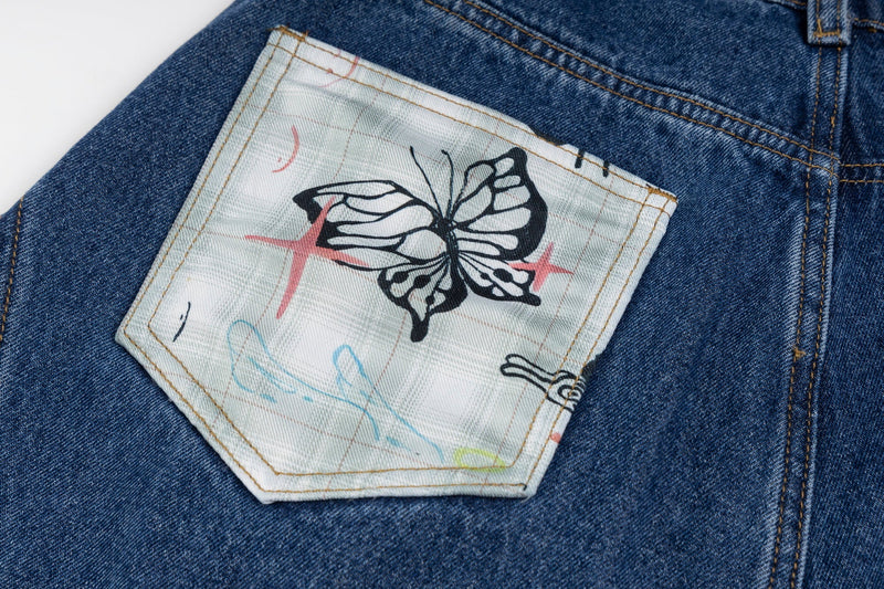Close-up of blue jeans back pocket with butterfly print patch and topstitching