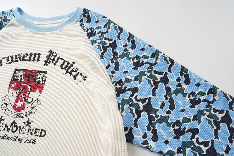 Three-quarter front view of cream raglan long sleeve tee with blue camo sleeves and streetwear crest graphic