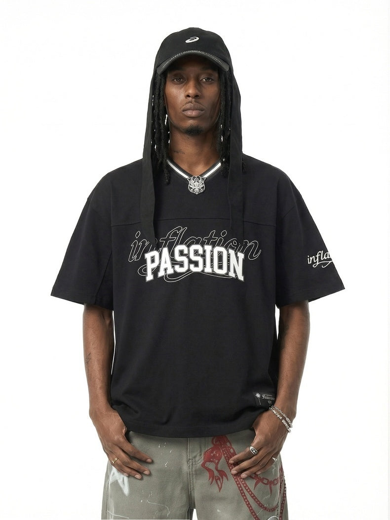 Black varsity streetwear V-neck tee with bold PASSION graphic, worn with a hooded cap and graphic pants on a model