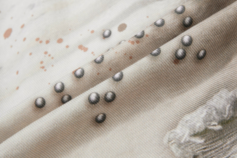Close-up of layered cream denim with painted splatter and raised silver studs