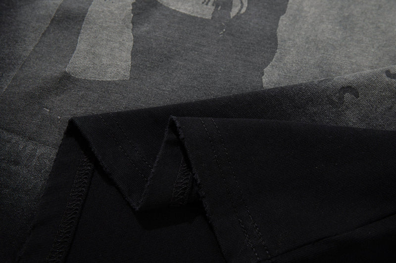 Close-up of washed black graphic T-shirt fabric with faded punk zine print and visible stitched hem detail