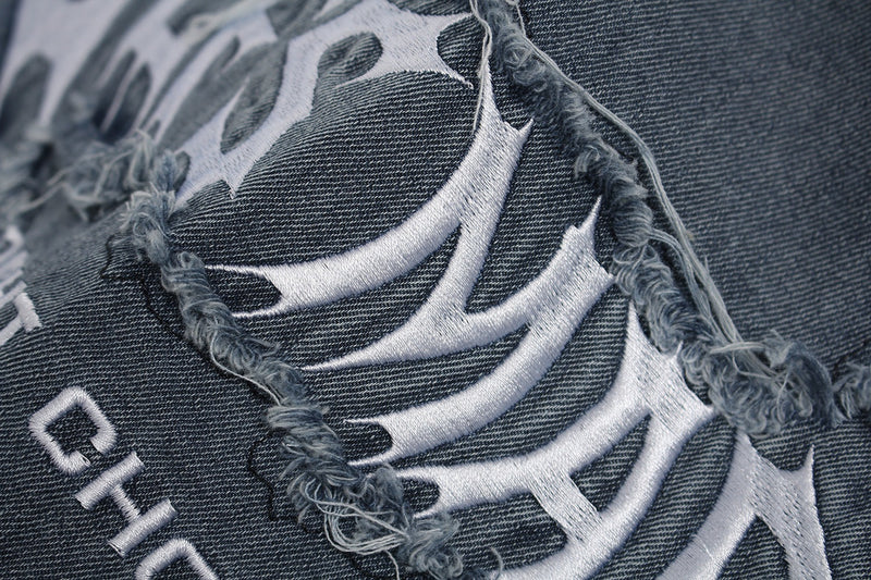 Close-up of dark washed distressed graphic T-shirt with frayed cutout detailing and white embroidered design