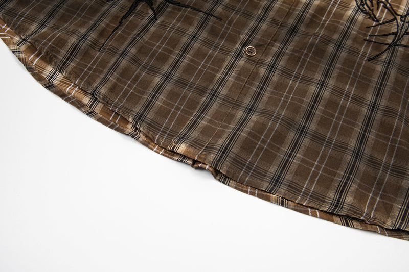 Close-up of a brown vintage plaid shirt hem with button detail and subtle graphic accents on white background