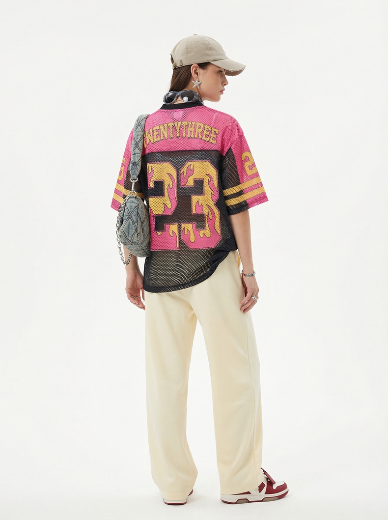 Model wearing a pink and black mesh football jersey with flame number 23, cream pants, and a beige cap, back view