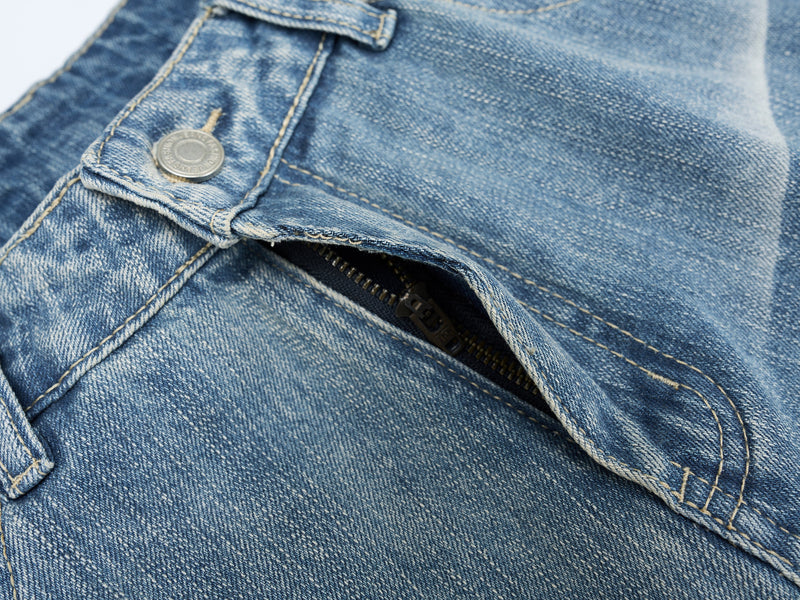 Close-up of front pocket and zipper area on blue washed denim jeans with visible stitching