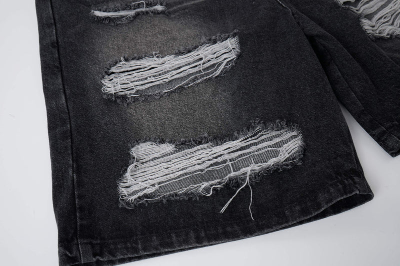 Close-up of black denim shorts with frayed ripped patches on the leg