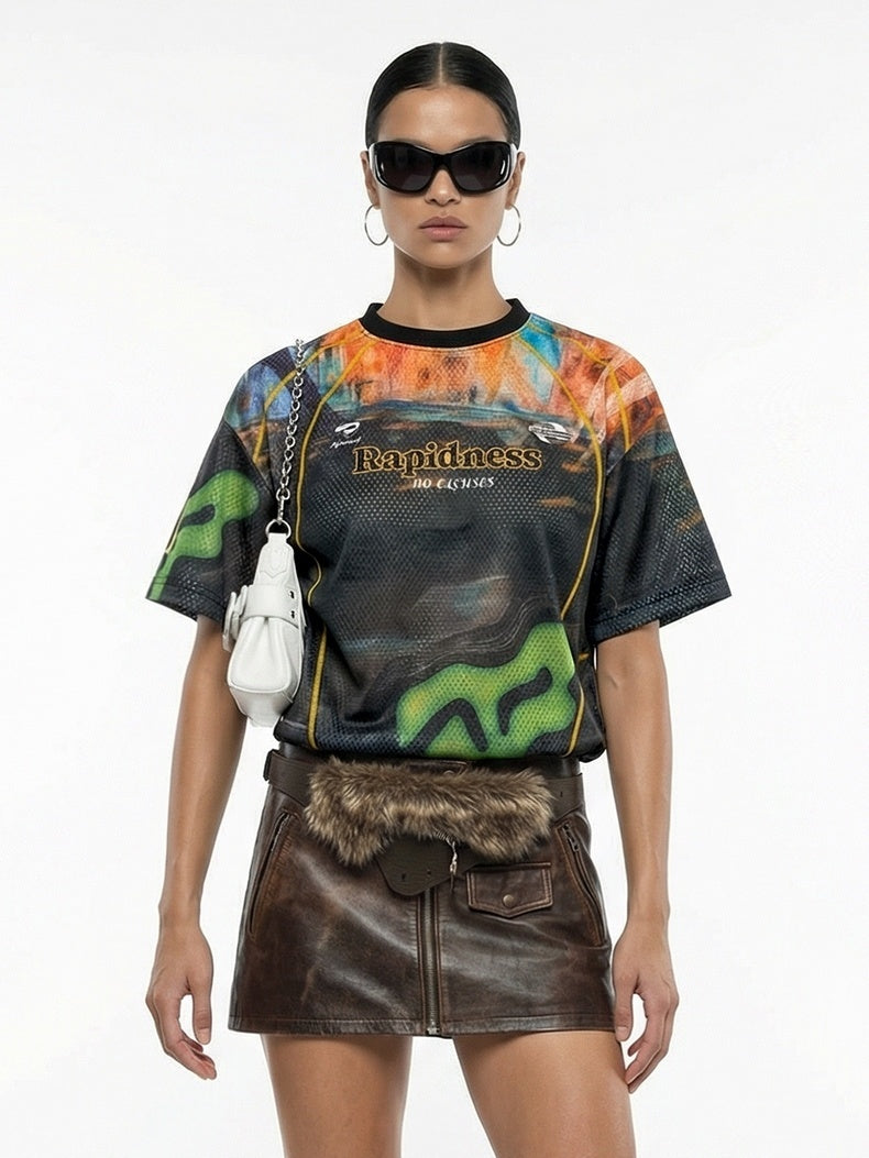 Model wearing a colorful racing mesh jersey with graphic print, paired with a brown leather mini skirt and white shoulder bag