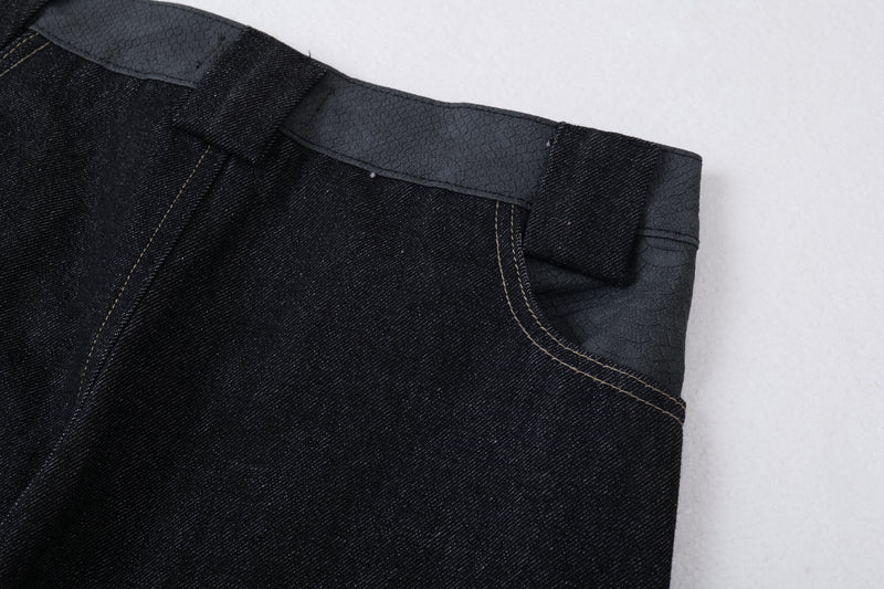 Close-up of the side waistband on dark denim jeans with textured trim and stitching