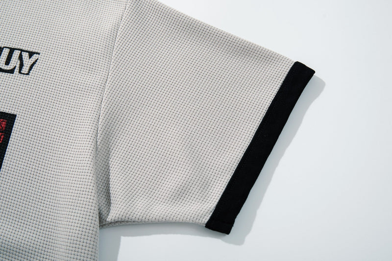 Close-up of a cream textured graphic T-shirt sleeve with black trim and partial punk-style print on the chest