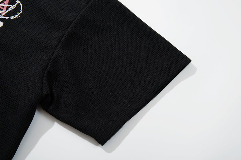 Black waffle-knit graphic tee sleeve with textured cotton fabric and punk-inspired print detail