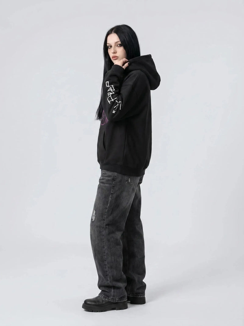 A person with long black hair wears the Lil Peep Hoodie — Sad Face Graffiti Graphic Sweatshirt, paired with loose dark jeans and black shoes, standing against a plain light grey background.