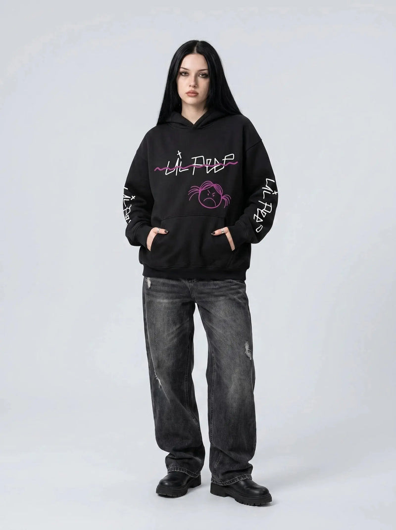 A person with long dark hair in a black Lil Peep Hoodie — Sad Face Graffiti Graphic Sweatshirt, loose dark jeans, and black boots stands against a plain light gray background.