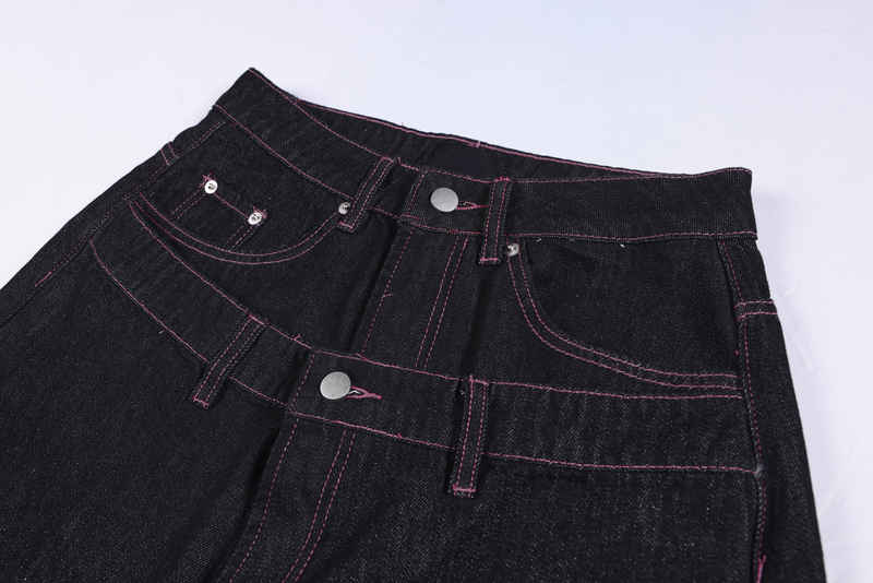 Close-up of the waistband and front pockets on black denim pants with pink stitching