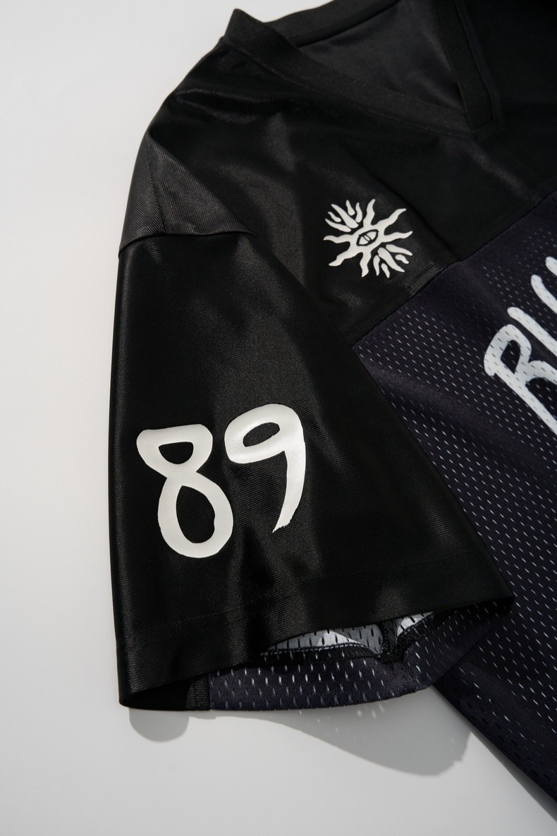 Black mesh football jersey with white 89 print and sunburst logo, shown in a close-up streetwear detail shot