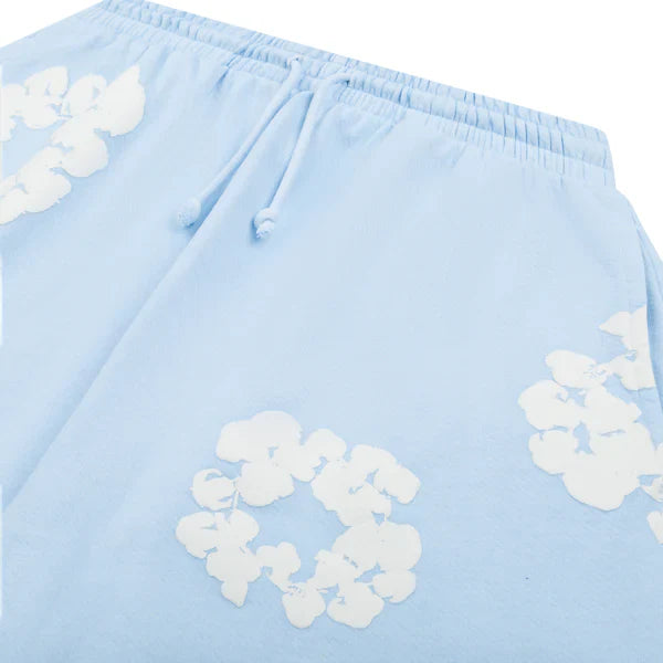 The Light Blue “Cotton Wreath” Denim Tears Sweatpants are streetwear pants with an elastic waistband, drawstring, and white floral print inspired by the iconic cotton wreath design.