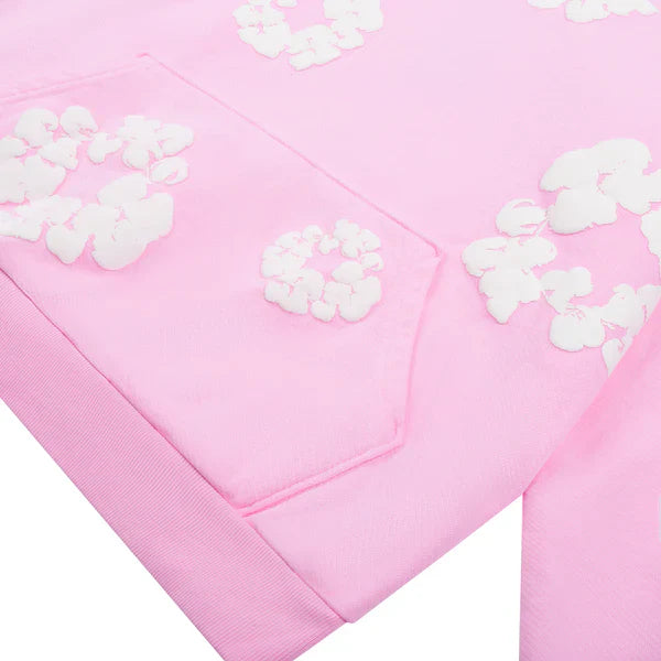 Close-up of the Pink “Cotton Wreath” Denim Tears Hoodie, featuring a light pink fabric pocket with raised white floral print. Visible texture and stitching add a trendy streetwear vibe inspired by classic Denim Tears style.