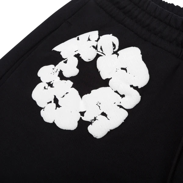 Close-up of Black “Cotton Wreath” Denim Tears Sweatpants, featuring a white floral print with a circular abstract design on black streetwear fabric, echoing the signature textured style.
