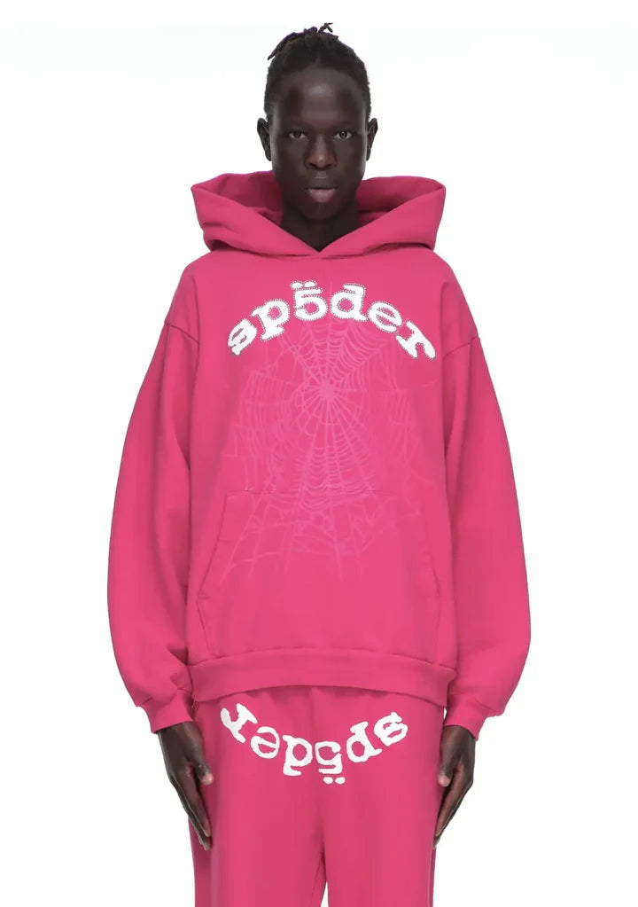 Wearing the Sp5der Web Hoodie – Hot Pink 440GSM Heavyweight Streetwear Pullover and matching sweatpants with white spiderweb graphics, a person showcases bold style against a plain white background.