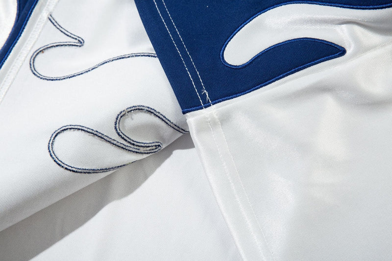 Close-up of white jersey sleeve and blue flame embroidery at the seam