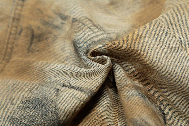Close-up of wrinkled denim fabric with tan and black spray-dye pattern