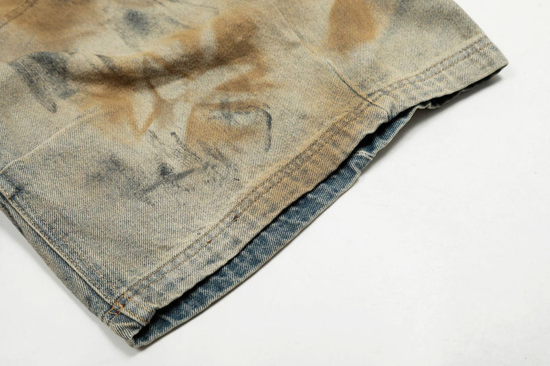 Close-up of folded hem on faded denim shorts with spray-dye markings
