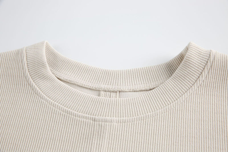 Close-up of cream ribbed tee with layered chest panel and structured crew neckline on a minimalist background