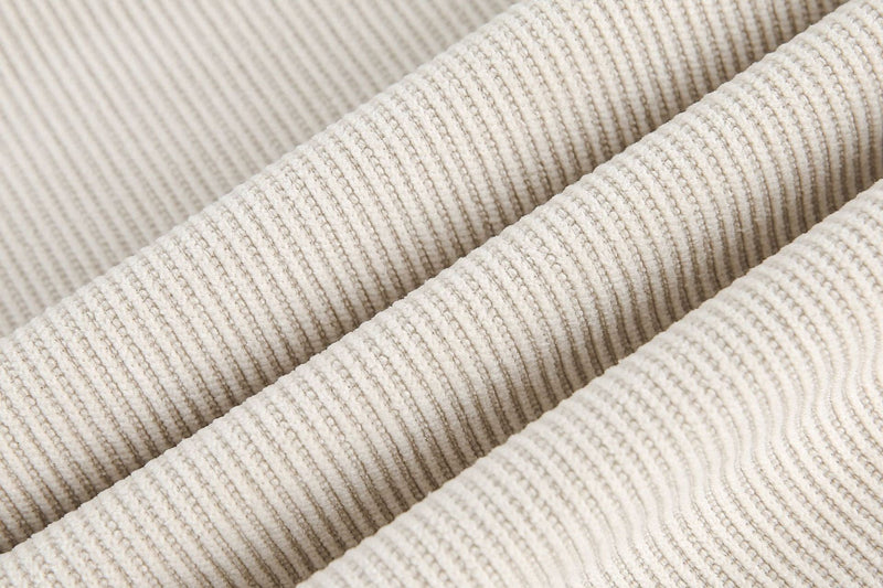 Close-up of beige ribbed fabric with layered texture and structured diagonal folds on a minimalist chest panel tee
