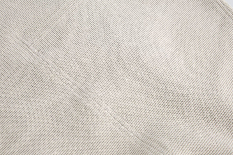 Close-up of a beige ribbed tee with layered chest panel detail and subtle structured seam texture