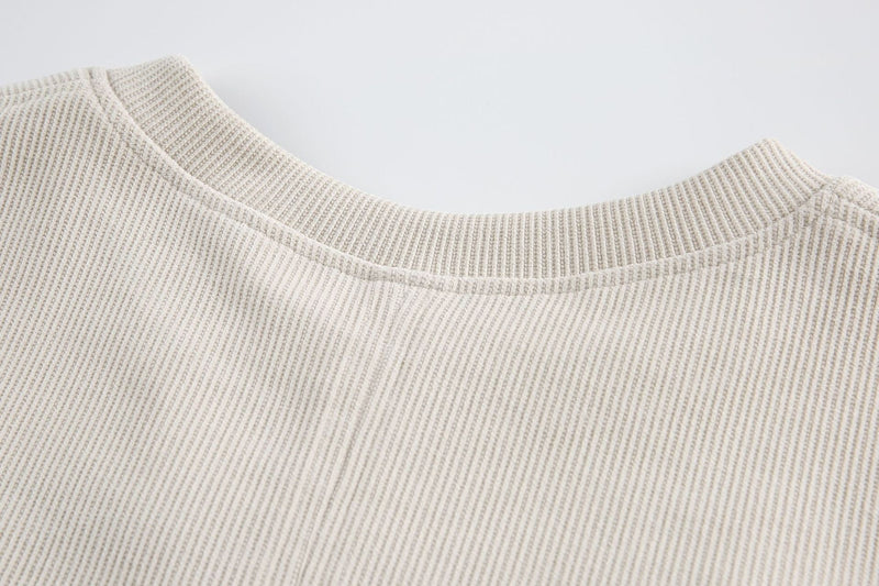 Close-up of an off-white ribbed tee with layered chest panel and structured crew neckline
