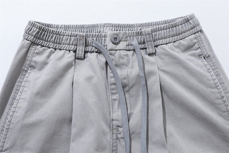 Close-up of light gray shorts waistband with button closure, drawstring, and belt loops