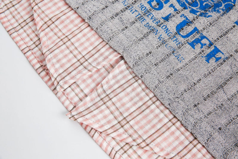 Close-up of a vintage streetwear tee with pink plaid collar mesh overlay and blue graphic print on gray fabric