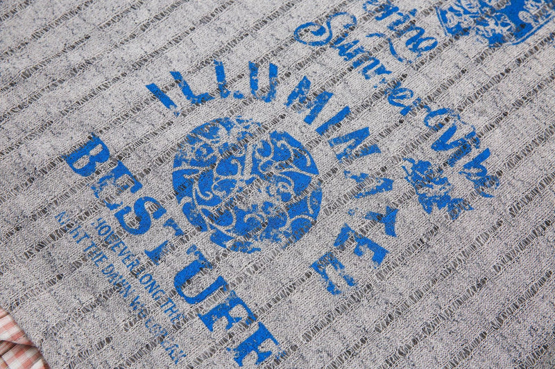Close-up of a gray mesh graphic tee with bold blue vintage lettering and a plaid collar detail