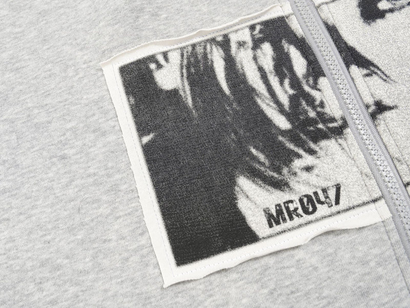 Close-up of the light gray hoodie chest patch beside the zipper with black-and-white portrait print