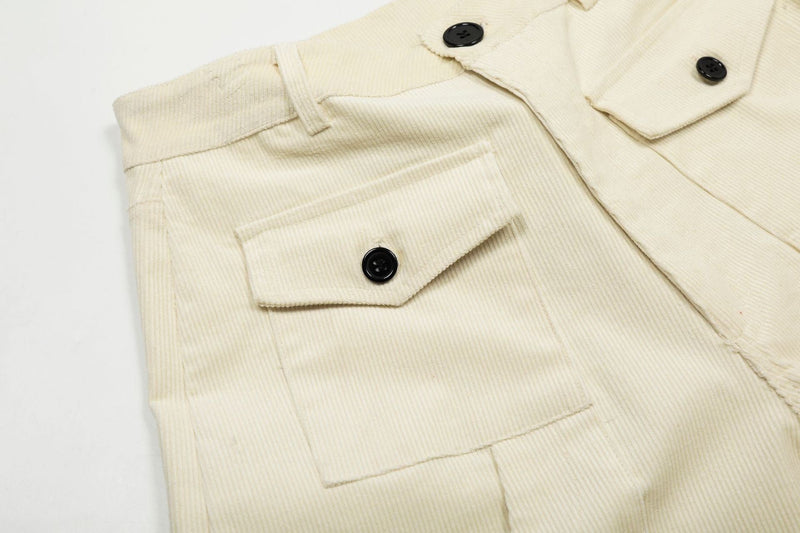 Close-up of cream corduroy shorts front pocket and waistband with black button details