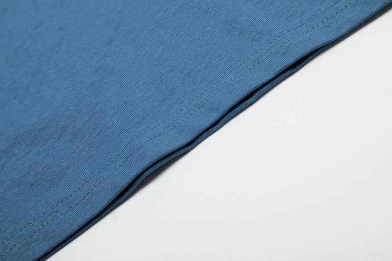 Close-up of blue oversized graphic T-shirt hem with visible stitching on a clean white background