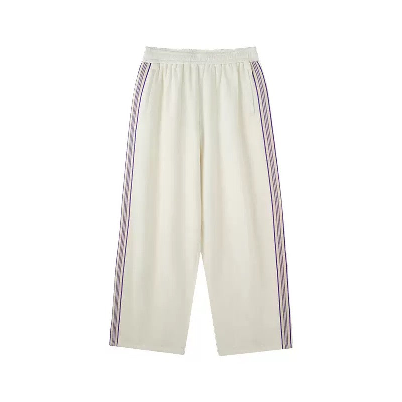 Cream wide-leg track pants with purple contrast side stripes and elastic waistband, laid flat on white background