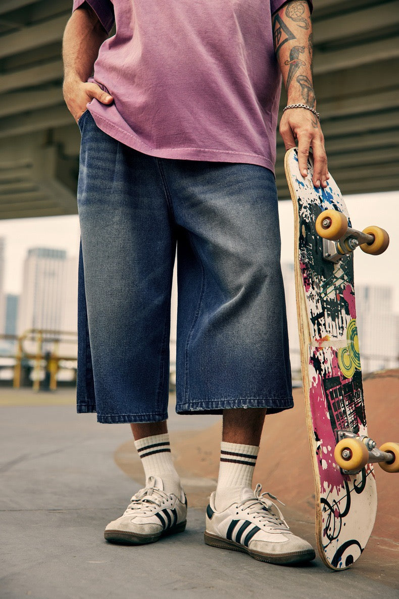 Close front view of dark denim shorts with wide legs and faded wash beside skateboard