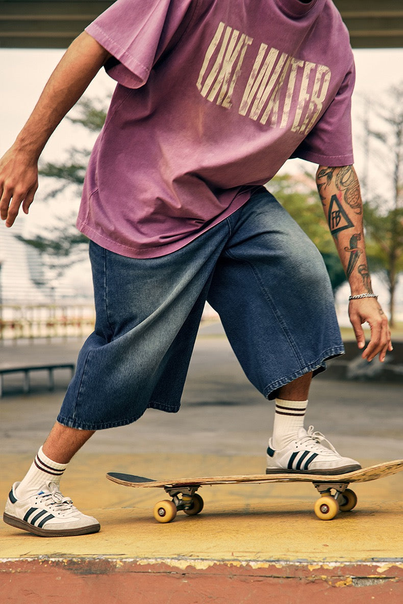 Model wearing wide-leg denim shorts in motion with skateboard and purple T-shirt